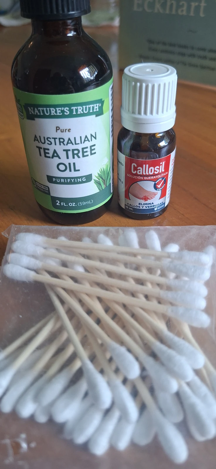 Tea tree oil bottle, Callosil keratolytic solution, and cotton swabs on a wooden surface